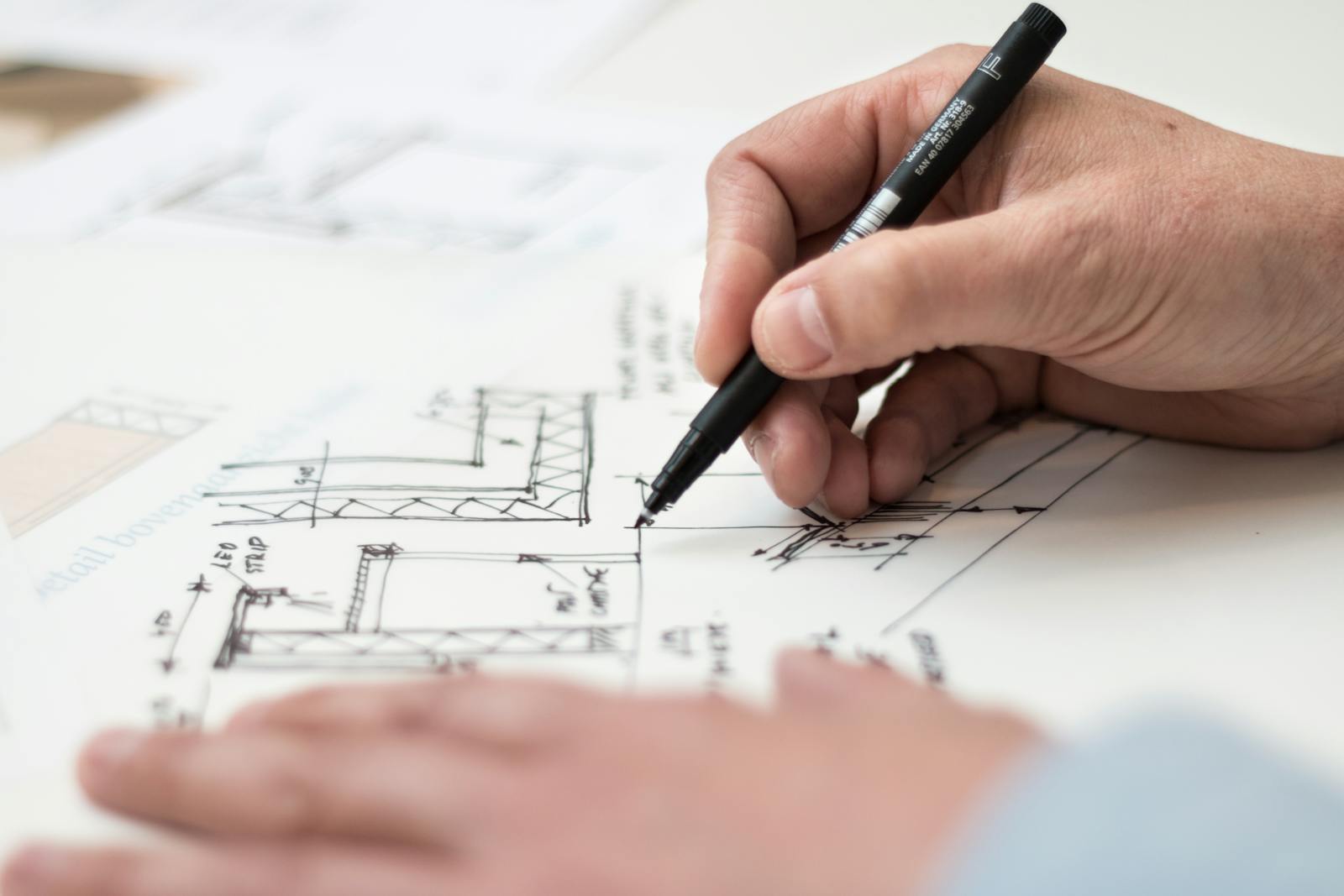 Photo by Lex Photography Close-up of hand drawing intricate technical designs on blueprint with pen, ideal for engineering or architecture themes.