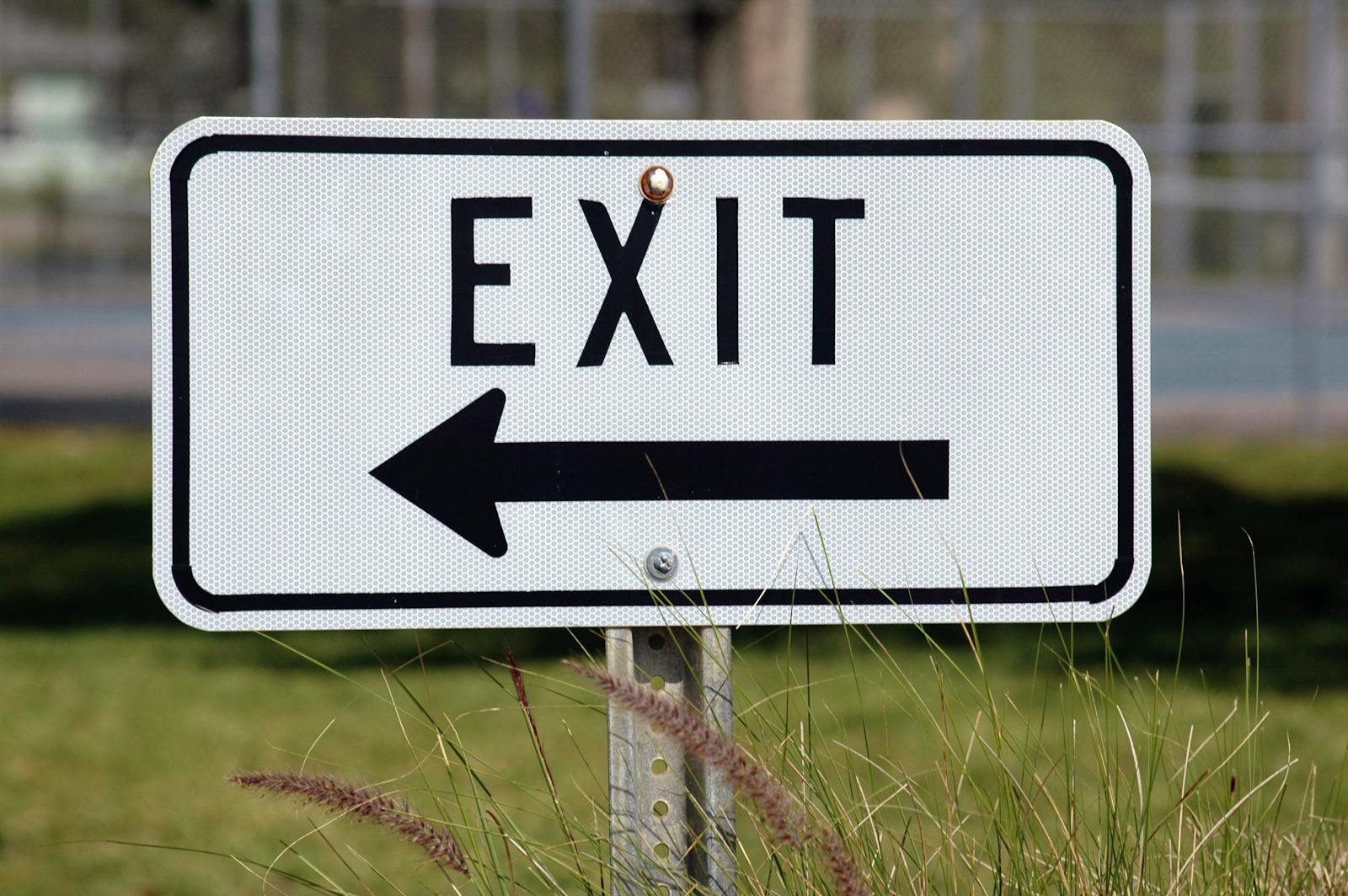 Photo by Pixabay Exit sign with left-pointing arrow in a grassy outdoor setting.