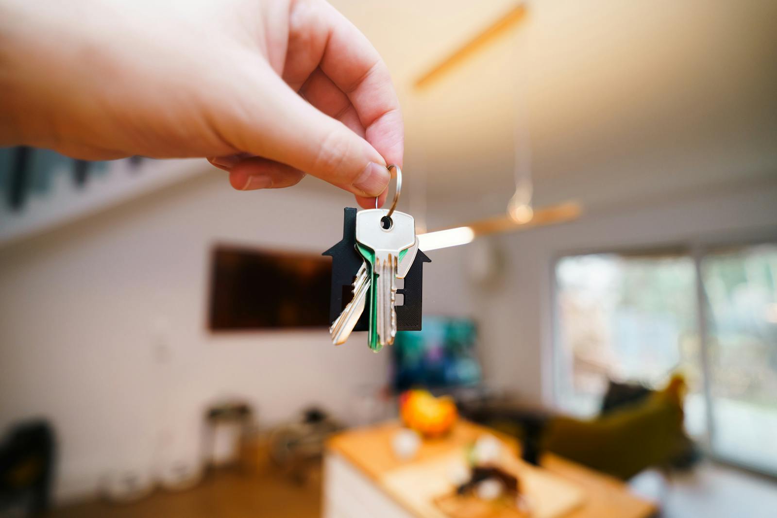 Photo by Jakub Zerdzicki A hand holds keys with a house keychain inside a modern, well-lit living space.