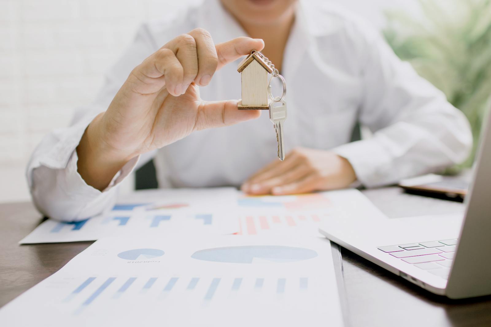 Photo by Khwanchai Phanthong Real estate professional presenting a house model with keys, symbolizing property investment and ownership.